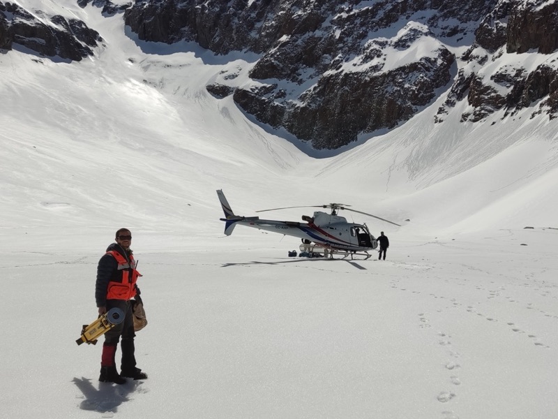 Profesional con instrumento topográfico junto a un helicóptero en un campo de nieve