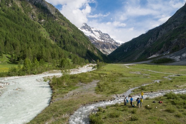 Valle fluvial de montaña con cauce trenzado y equipo en terreno